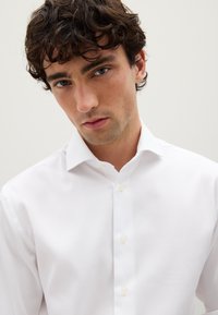Witte button-up shirt van gladde stof, met een klassieke kraag en subtiele textuur, met zichtbare knopen aan de voorkant.