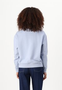 Sweatshirt de algodão azul claro com um corte descontraído, punhos e barra canelados. Combinado com calças largas de denim escuro.
