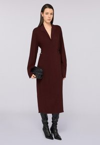 Bordeaux wrap jurk met lange mouwen en een V-hals. Heeft een gestructureerde zwarte clutch en strakkere zwarte kniehoge laarzen. Gladde stofafwerking.