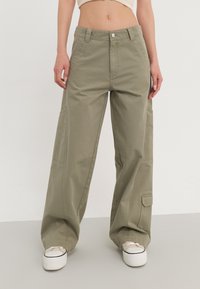 Pantalons cargo à larges jambes en vert olive, avec une taille haute, des poches avant et des poches à soufflet sur les côtés. Fabriqués en tissu coton robuste.