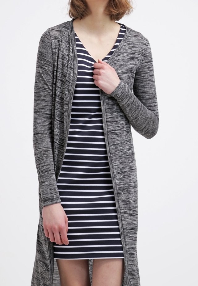 Femme portant une robe à rayures horizontales noires et blanches et un long cardigan gris ouvert sur le devant.