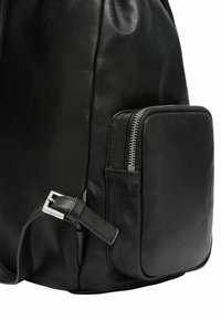 Czarny skórzany plecak o gładkiej fakturze, wyposażony w boczną kieszeń na zamek błyskawiczny oraz regulowany pasek z srebrnymi elementami metalowymi.