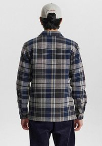 Checkered flannel shirt in navy, grey, and white with button cuffs and a collar. Soft texture with a visible plaid pattern.