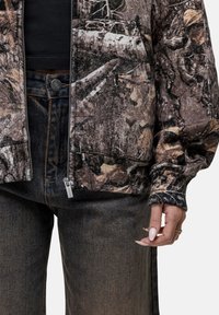 Giacca in pile con motivo camouflage, dotata di chiusura con zip, polsini a costine e tasche frontali, abbinata a jeans in denim scuro con taglio dritto.