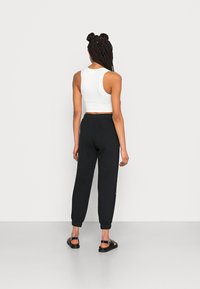 Vit ribbad crop top och svarta joggers med elastiska muddar, visad bakifrån; modellen har på sig platta sandaler med spänne.