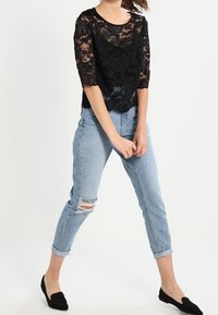 Top in pizzo nero con maniche a tre quarti, abbinato a jeans strappati azzurri e ballerine nere. Design in pizzo testurizzato con motivi floreali.