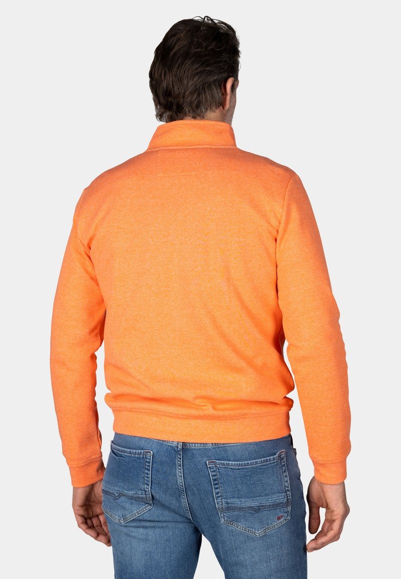 Pomarańczowy sweter z wysokim kołnierzem, teksturowana tkanina i ściągacze na rękawach, w zestawieniu z niebieskimi dżinsami z tylnymi kieszeniami.