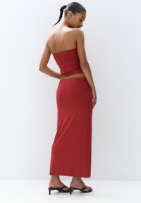 Ensemble rouge deux pièces comprenant un haut sans bretelles ajusté et une longue jupe fluide. Fabriqué à partir d'un tissu lisse, avec un design épuré et minimaliste.
