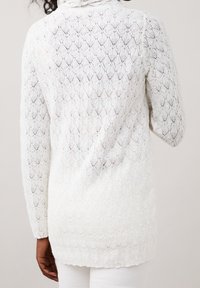 Lungo maglione bianco in pizzo con motivo a diamante, caratterizzato da una vestibilità ampia e maniche lunghe, realizzato in un materiale lavorato a maglia leggero.