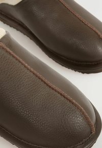 Brūni ādas čības ar teksturētu apdari, ar kontrastējošām brūnām šuvēm gar centrālo šuvi un noapaļotu purngalu.