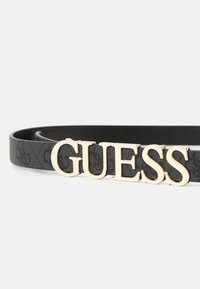 Ceinture synthétique noire avec une surface texturée et un grand logo doré "GUESS" en accent de boucle.