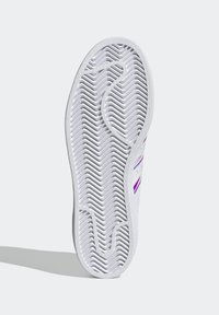 Vit sneakersula med en texturerad gummidesign och zigzagmönster. Inkluderar färgade accenter i lila och blå längs sidan.