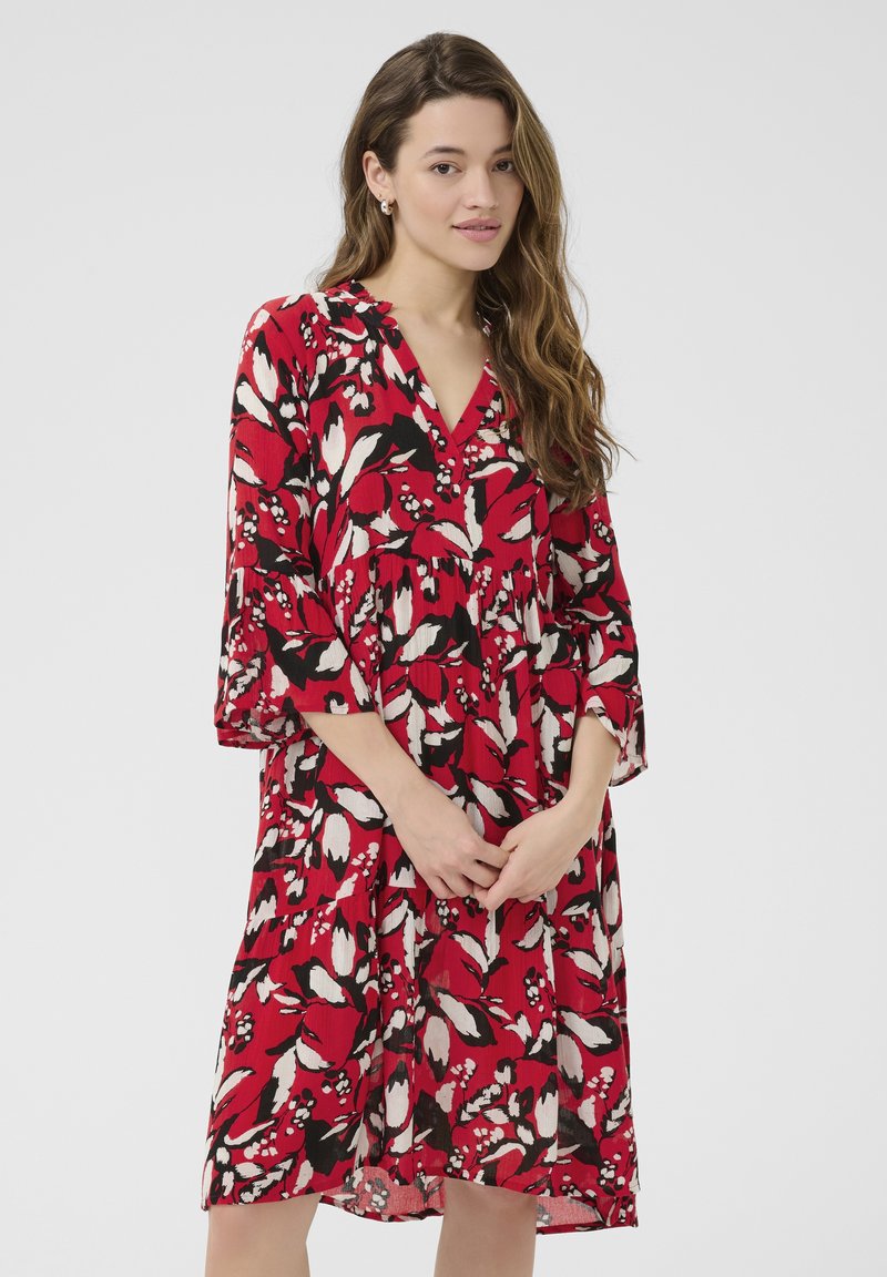 Robe florale rouge avec des accents noirs et blancs, décolleté en V et manches trois-quarts, fabriquée dans un tissu léger avec un design fluide.