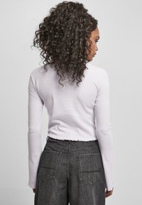 Fialový top s dlouhým rukávem s cropped designem, ribrovou texturou a detaily s surovým lemem, kombinovaný s tmavě šedými džínami s vysokým pasem a zadními kapsami.