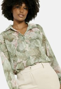 Long-sleeve, lightweight blouse in a sheer, green and pink floral pattern with a button-down front and a classic collar.