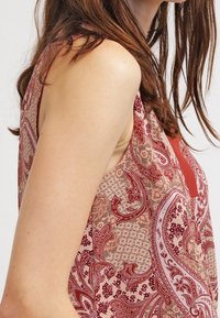 Top senza maniche con un motivo paisley in tonalità di rosso caldo e beige, con scollo a V e tessuto strutturato. Finitura liscia.