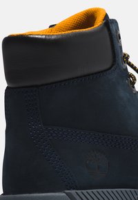 Morska zamszowa boot z czarnymi skórzanymi akcentami, jasnobordowym podszewkiem i starannie wykonanym haftem. Posiada markowy logotyp po boku.
