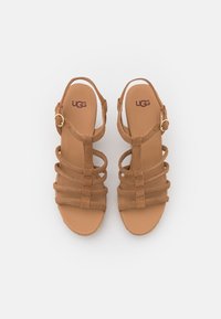 Bruine suède sandalen met meerdere banden, platte hak en een gesp-sluiting. De binnenzool heeft een merklogo en een gladde textuur.