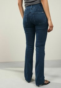 Vaqueros de campana azul oscuro confeccionados en denim, con una cintura de altura media, bolsillos frontales y traseros, y sutiles detalles de costura.