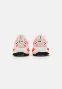 Zapatillas de running Nike en blanco, rosa y negro. Parte superior de malla con patrón a rayas, cuello acolchado y suela de goma para mayor tracción.