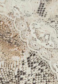 Närbild av krämfärgad spets med lager ovanpå ormskinnstrykt textil i beige, bruna och svarta toner.