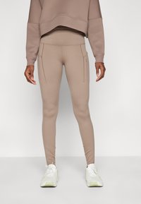 Leggings a vita alta in tessuto stretch color marrone chiaro con cuciture piatte e due tasche laterali. Abbinati a una felpa cropped coordinata.