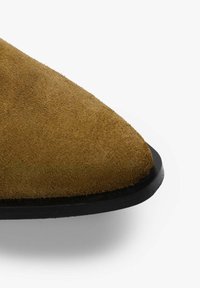 Zapato de ante color marrón claro con puntera afilada y suela de goma negra. La superficie tiene una textura suave, con un acabado liso sin costuras visibles.
