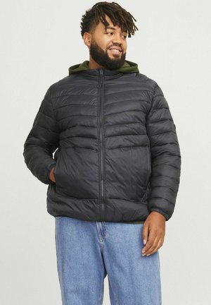 Sort pufferjakke med vandret quiltet mønster, lynlåslukning og fastgjort grøn hætte; parret med lyseblå jeans.