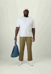 White t-shirt, khaki pants, white sneakers, beige cap, holding a blue fabric tote bag. Simple design with relaxed fit. Plain background.