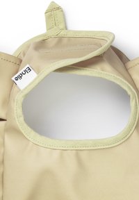 Prodotto in tessuto beige con un ritaglio arrotondato, bordato di verde chiaro. Presenta un'etichetta con il nome del marchio visibile nell'angolo in basso a sinistra.