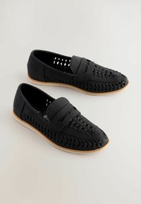 Chaussures noires de style mocassin avec un design tissé et une semelle en caoutchouc plate. Présente un bout arrondi et une bande en cuir lisse sur le dessus.