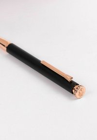 Svart penna med en slät yta, roséguld accenter, en klipp, och ett dekorativt lock med ett mönster som har små stenar.