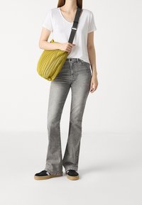 Sac à bandoulière rayé jaune en tissu texturé, associé à un T-shirt blanc et un jean gris évasé, ainsi qu'à des baskets noires avec une semelle en caoutchouc.