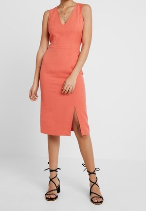 Hihaton korallinen polvipituinen mekko sivuhalkiolla, yhdistetty mustiin remmikkäisiin lohkokorkokenkiin ja kerroksellisiin kultakoruisiin kaulakoruihin.