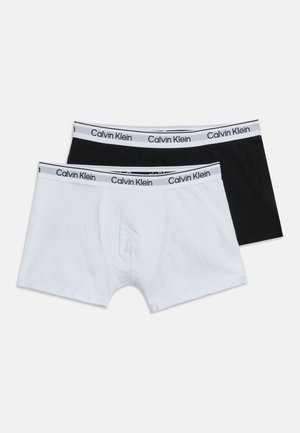 Dva páry pánskych boxeriek Calvin Klein, jedny čierne a jedny biele, s bielymi pásmi v páse s logom značky.