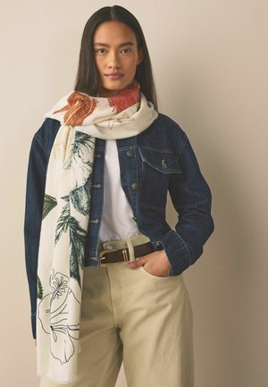 Schal mit Blumenmuster in Creme, mit roten und grünen Motiven. Wird über einer blauen Jeansjacke mit figurbetonter Silhouette und einem braunen Gürtel getragen.