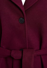 Burgundy wool coat featuring a notch lapel, two black buttons, and a tied waist belt. Smooth texture with a structured design.