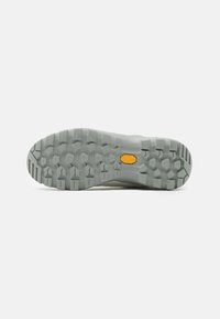 Suela de goma Vibram en gris claro con tacos multidireccionales para tracción. Presenta un logo amarillo. Diseño plano, superficie texturizada.