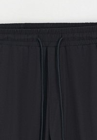 Pantalons de jogging noirs, légers, avec une taille élastique et un cordon de serrage ajustable. Présente une texture lisse et sans motifs visibles.