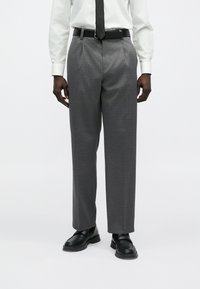 Hallid mustriga püksid, mille lõige on lõdvestunud ja mis on valmistatud kergest kangast, kantud valge särgi ja mustade kingadega. Lisatud must vöö.