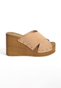 Tan suède wedge sandalen met kruislingse bandjes en gouden studs. Houten platform basis, open teen ontwerp en zachte textuur.