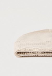 Căciulă bej tricotată, cu boră pliabilă, având textură zigrinată și material moale de lână, prezentând un design simplu, neîmpodobit.