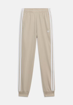 Beige atletikbukser med elastisk taljebånd, to forlommer, hvide sidelommer og lille hvid Adidas-logo på venstre lår.