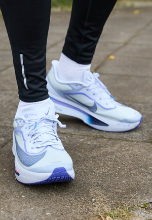 Svijetloplave atletske cipele s mrežastim gornjim dijelom, ljubičastim detaljima i teksturiranim potplatom. Šnirevi i reflektirajući Nike logotip su vidljivi.