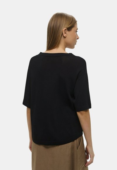 Top nero a maniche corte con una vestibilità ampia, scollatura rotonda, texture liscia e un design semplice, abbinato a una gonna marrone chiaro.