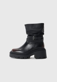 Sort læderankelstøvle med en slouchy overdel, spænde detaljer og en tyk, robust sål. Har rund tå og glat tekstur.