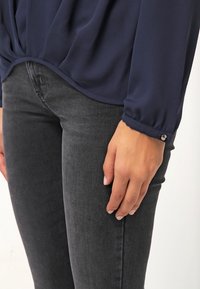 Námořnická blůza z měkkého, splývavého materiálu se sbíraným detailem v pase, doplněná tmavě šedými upnutými džíny a stříbrným knoflíkem na manžetě.