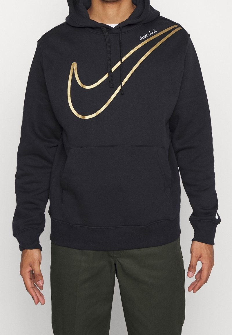 Musta Nike huppari, jossa on suuri kultainen swoosh-logo ja "Just do it" -teksti, kengurupussitasku ja nyörihuppu.