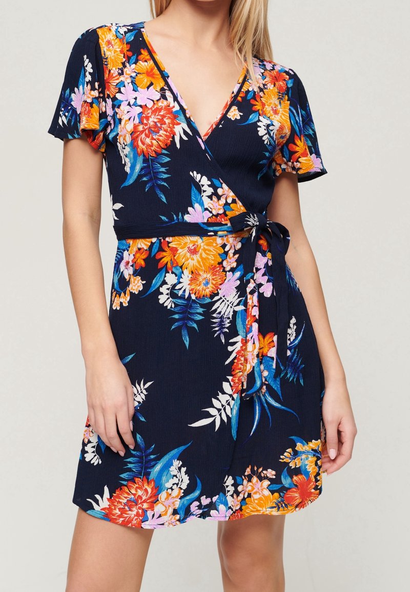 Blommig ombreklänning i marinblått med korta ärmar, med ljusa orange, rosa och vita blommor. Slät tyg med en knytning i midjan.