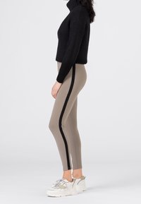 Leggings beige con strisce laterali nere, tessuto elasticizzato, design a vita alta. Abbinati a un dolcevita nero a costine e sneakers chunky bianche.
